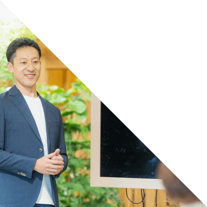 紺のジャケットを着た男性が笑顔でプレゼンテーションを行っている様子