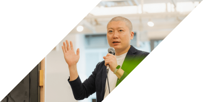 マイクを持ち片手を上げながら力強くスピーチする男性の様子